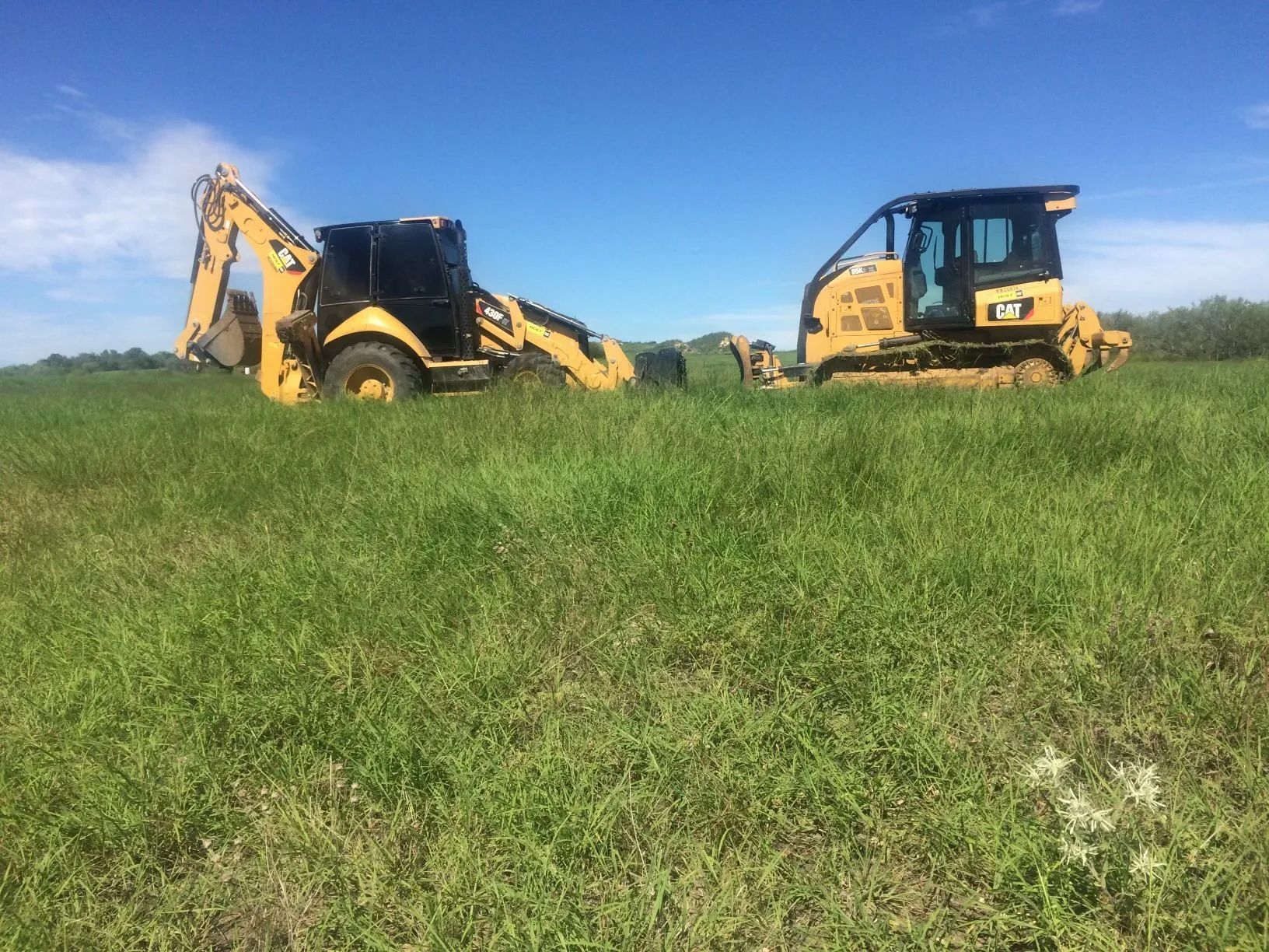 A bulldozer and a backhoe are parked in a grassy field.