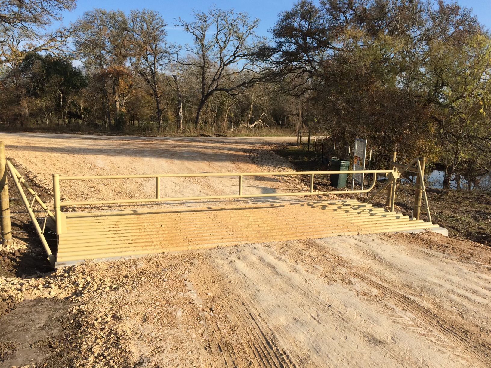 A wooden bridge over a dirt road with trees in the background.