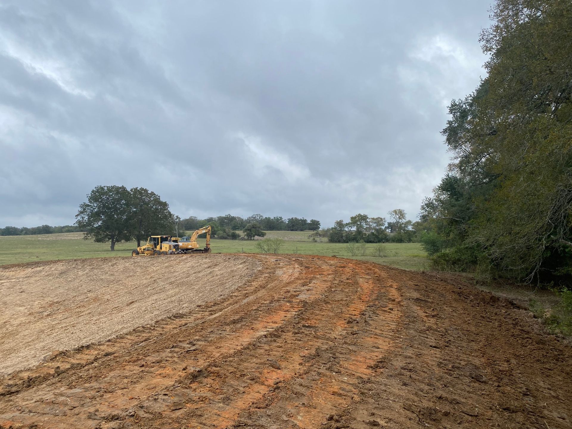 A bulldozer is plowing a dirt field on a cloudy day.