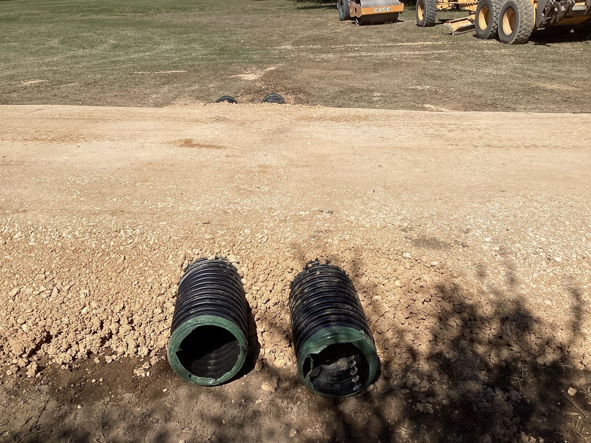 Two drain pipes are sitting in the dirt in a field.