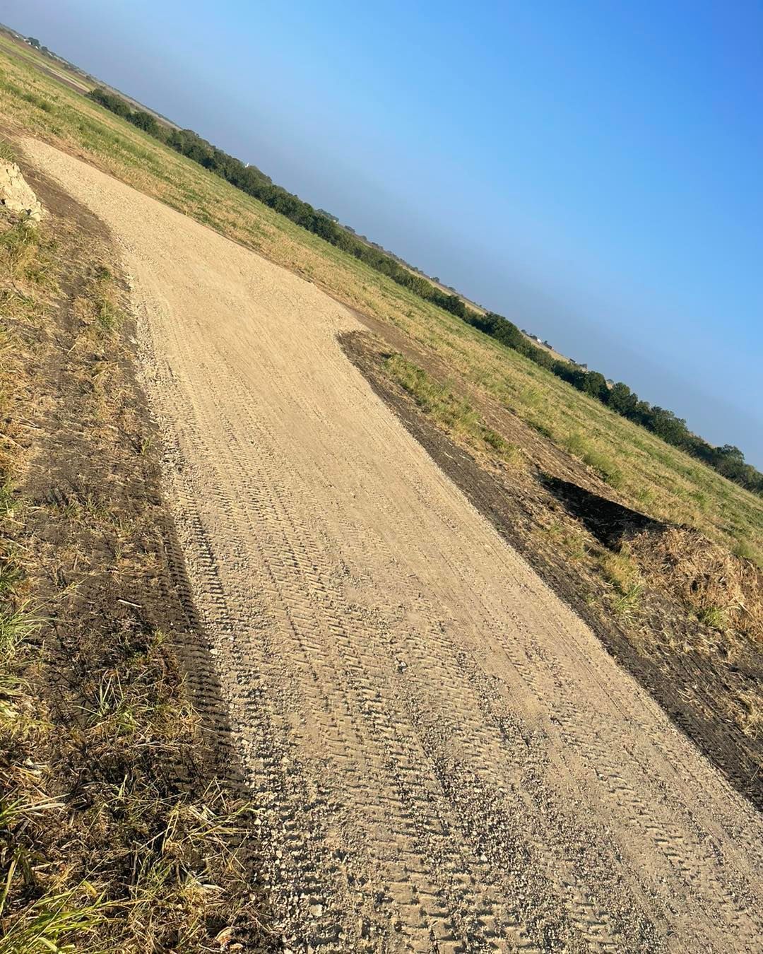 A dirt road going through a grassy field with a blue sky in the background.
