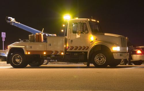 Tow truck at night, lights on, assisting a car.
