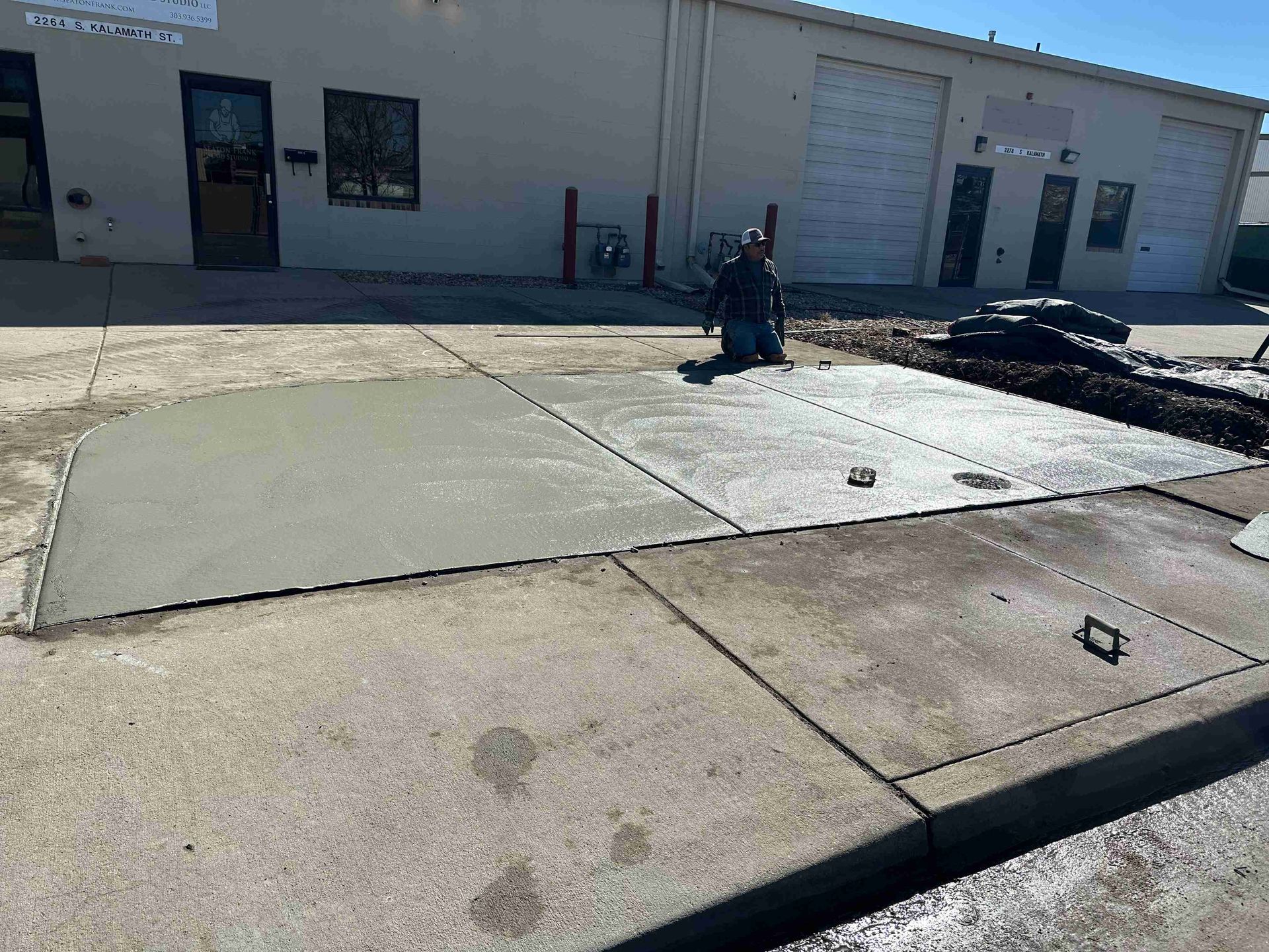 Concrete sidewalk and curb by a beige industrial building with a garage door and a fire hydrant.