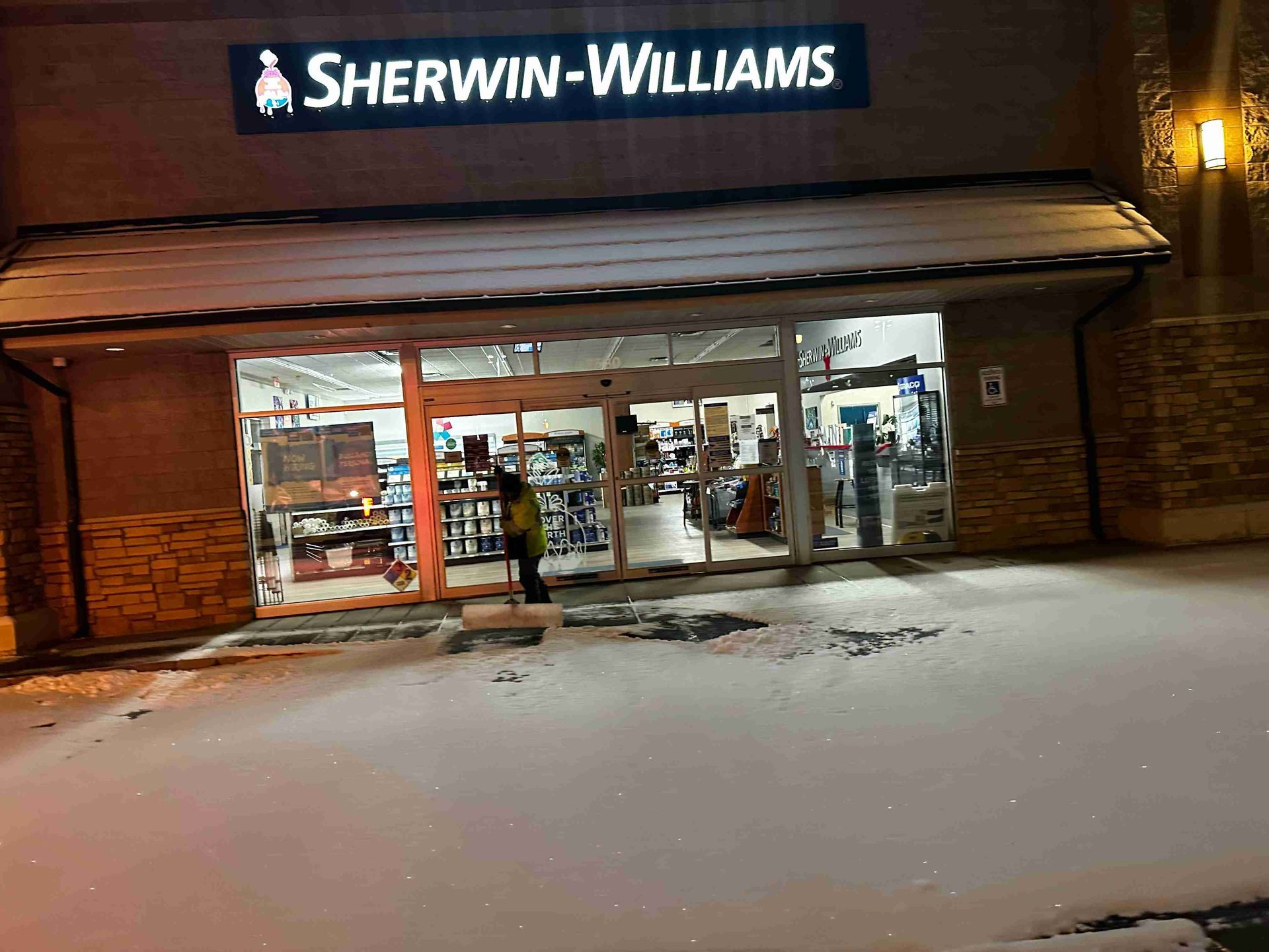 Sherwin-Williams storefront at night with snow-covered sidewalk and lit windows