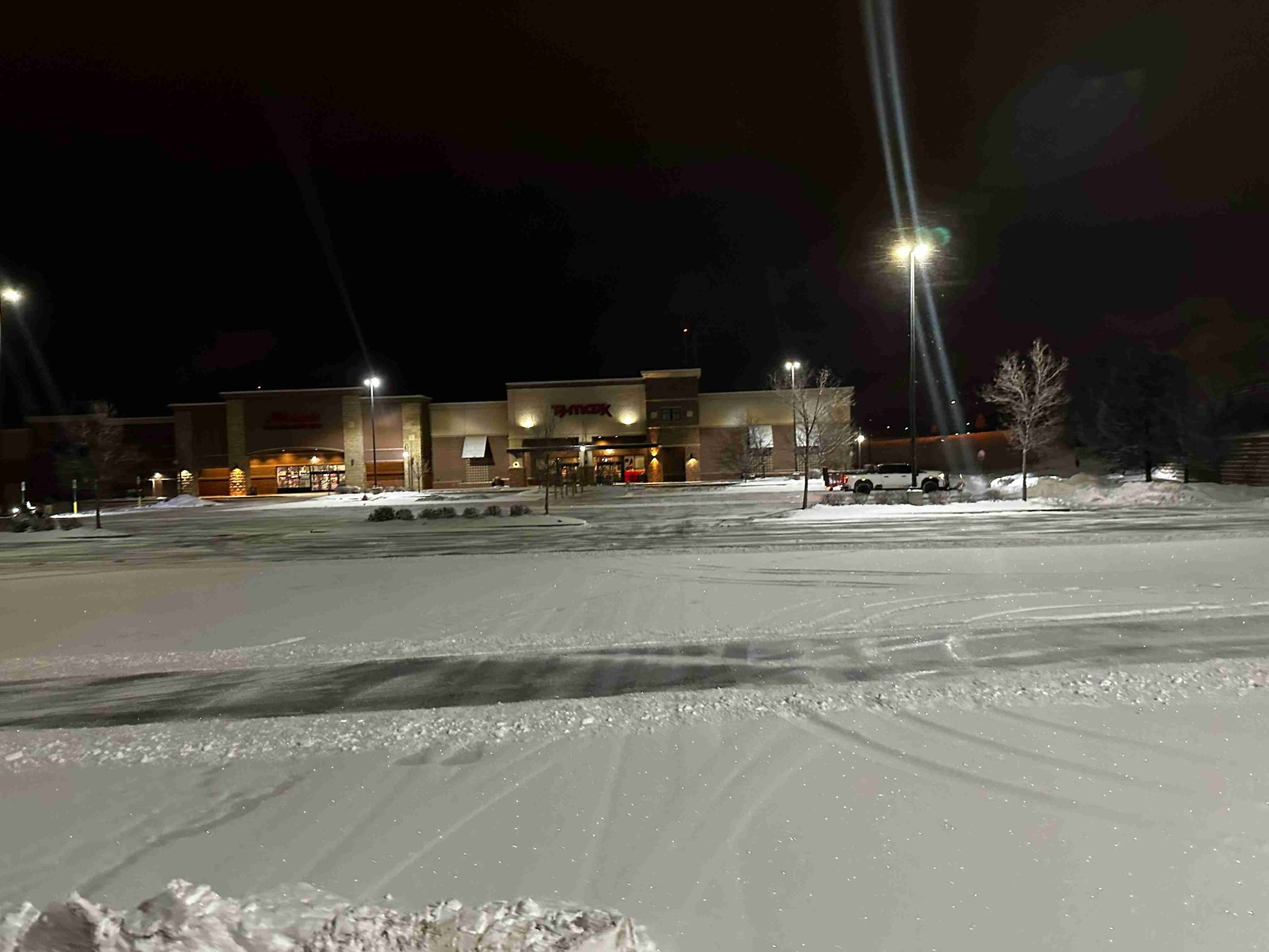 Snow-covered parking lot at night with lit buildings and streetlights in the background