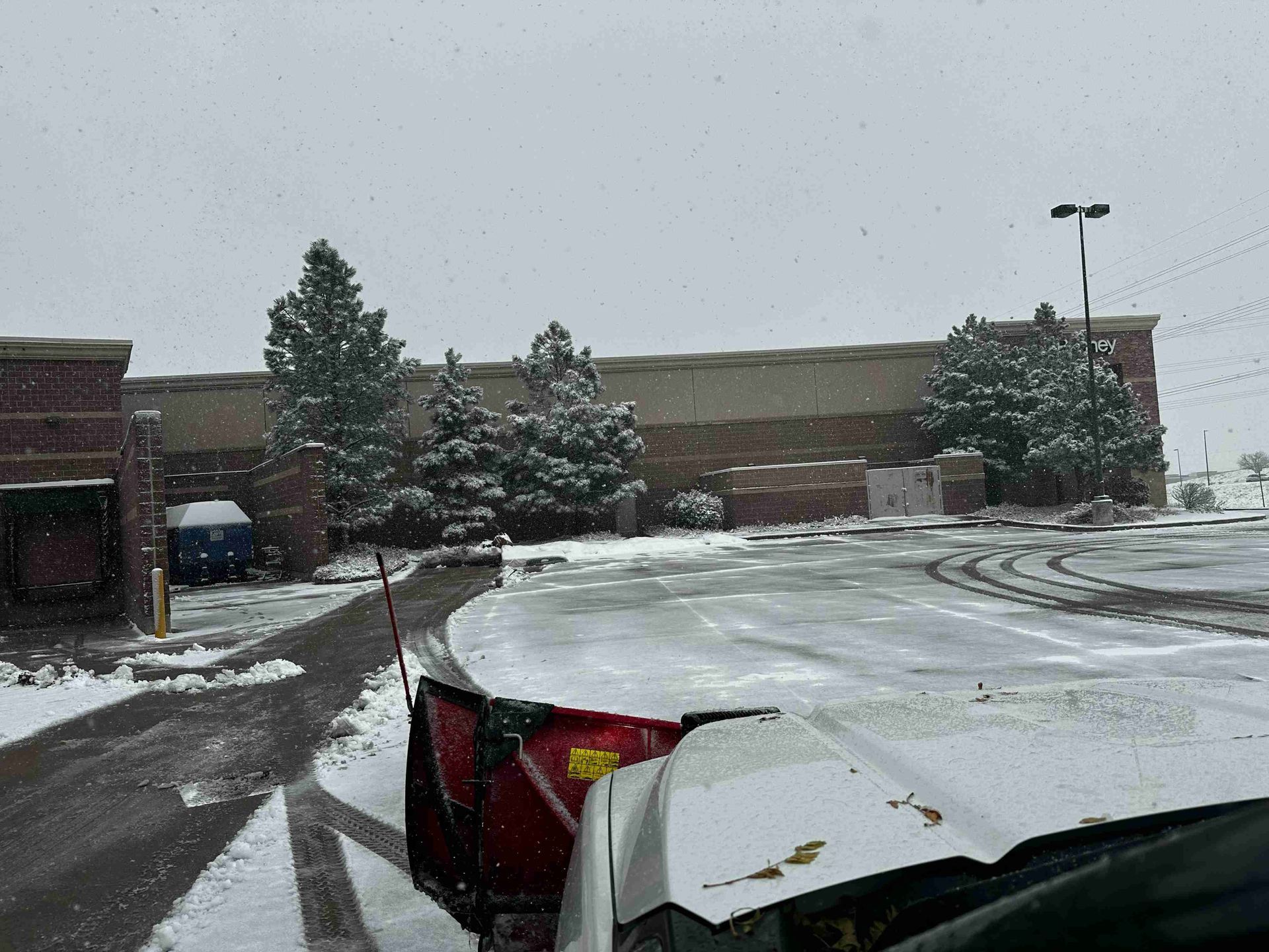 Snow-covered parking lot with a damaged white car in the foreground and a brick building in the background