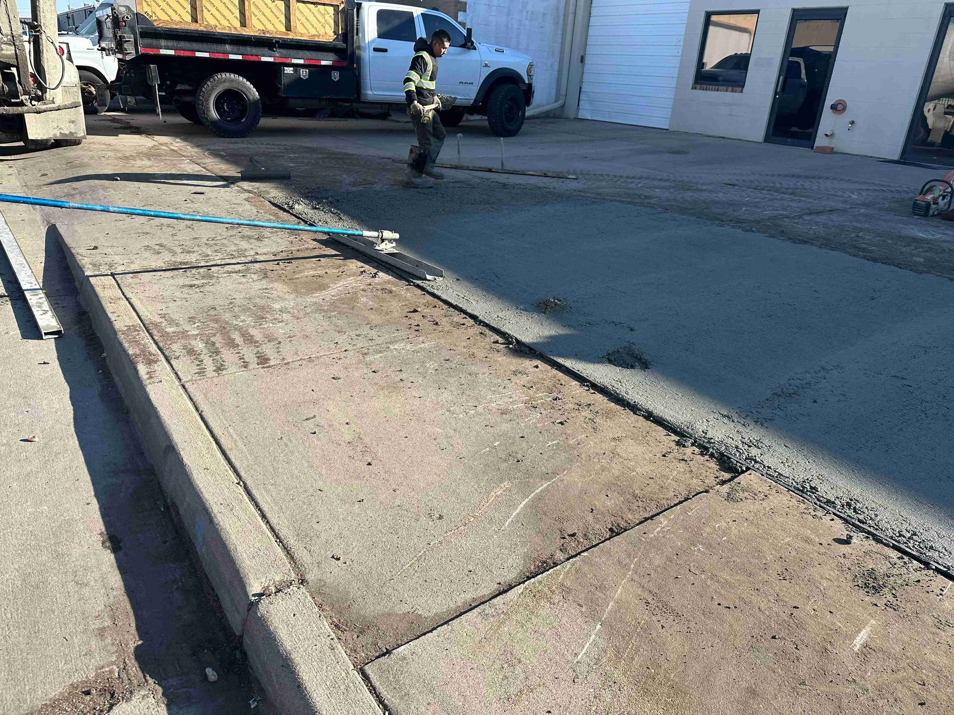 Damaged concrete sidewalk beside a truck and worker near a building and driveway