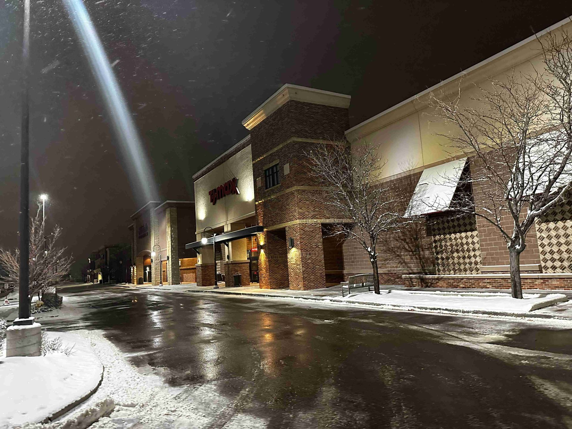 Snowy shopping center parking lot at night with wet pavement reflecting lights