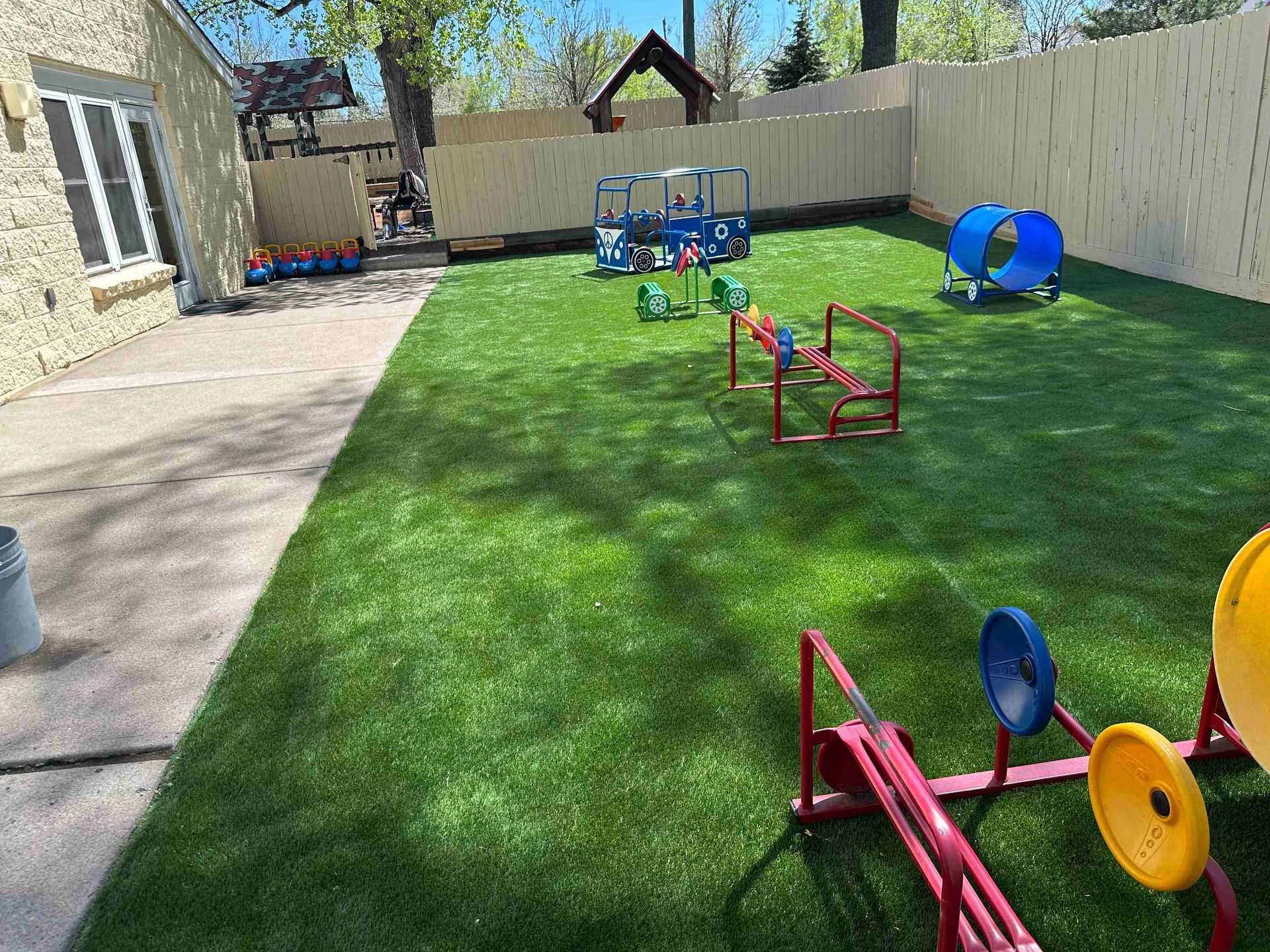 Backyard with artificial turf, small playground equipment, and a concrete walkway along a fence.
