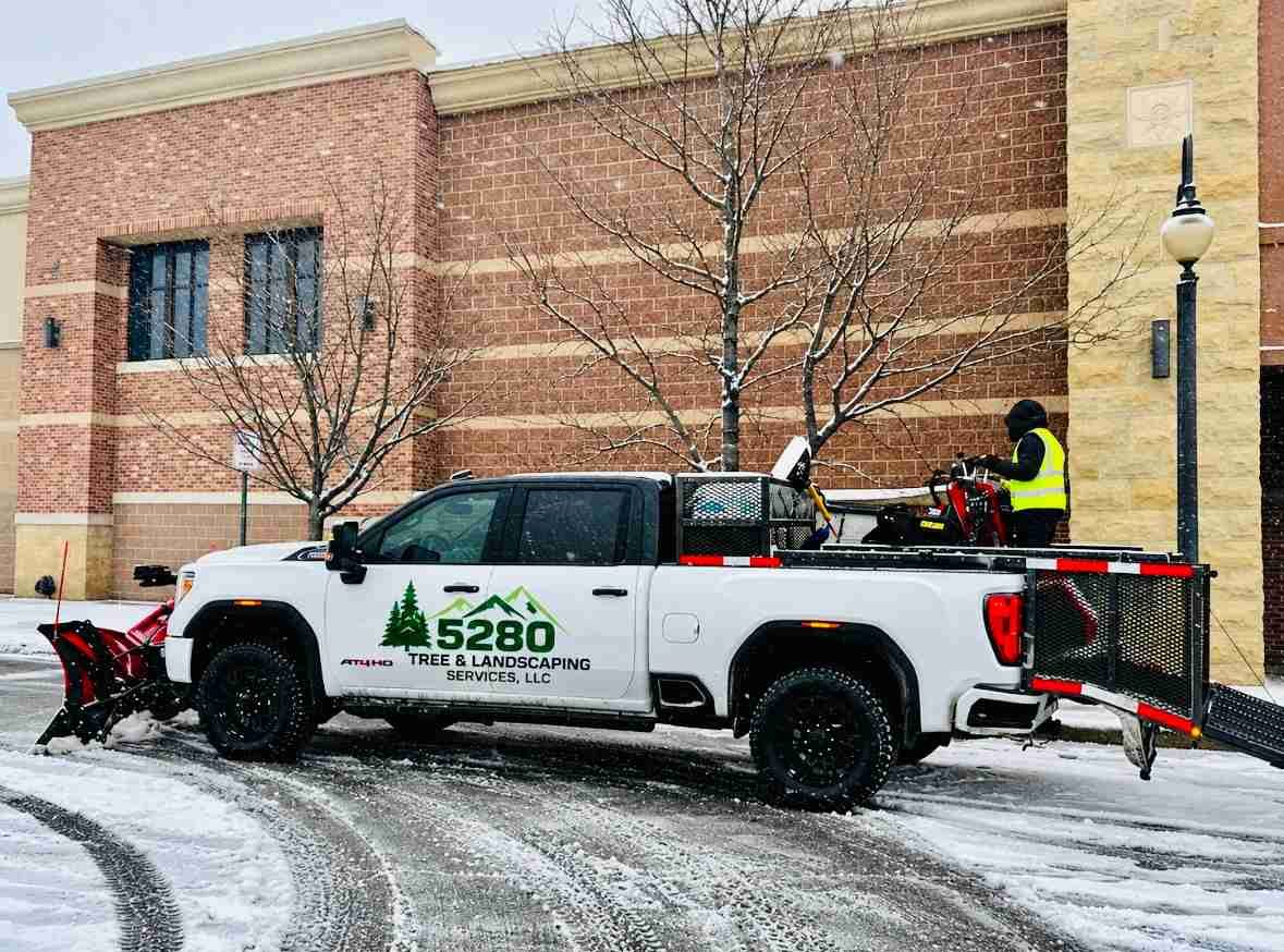 Snow removal crew using pickup truck and plow outside a brick building in winter