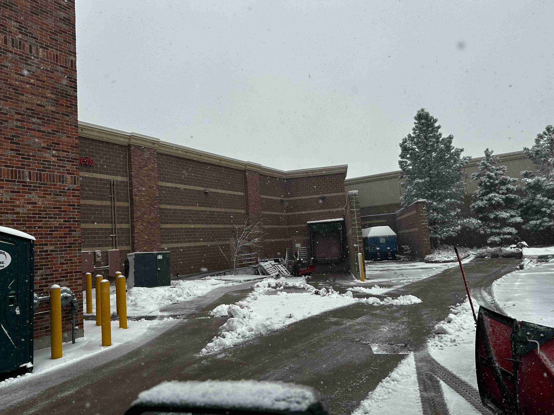 Snowy alley beside a brick building with parked cars and yellow bollards