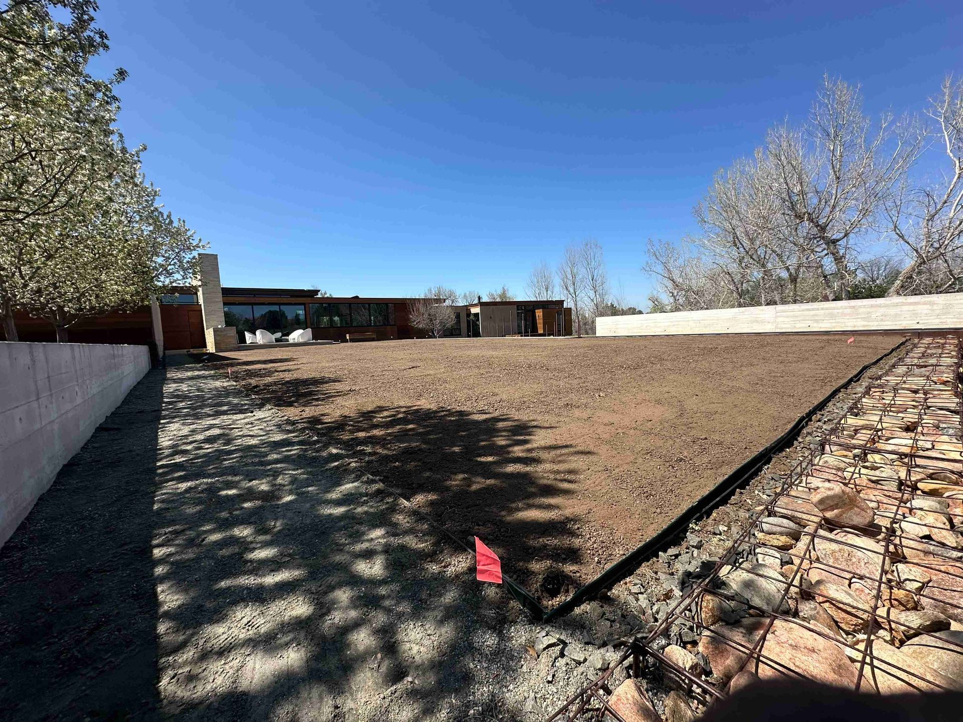 Dry landscaped yard with gravel, low retaining walls, and trees under a clear blue sky