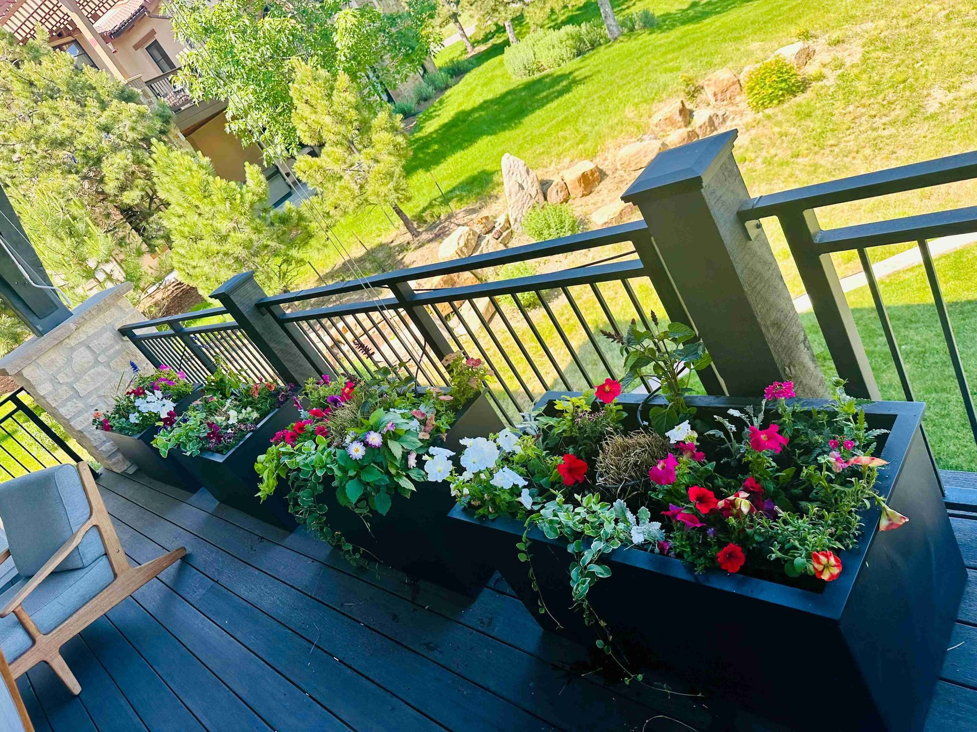 Deck with colorful flower planters beside a black railing overlooking a green garden