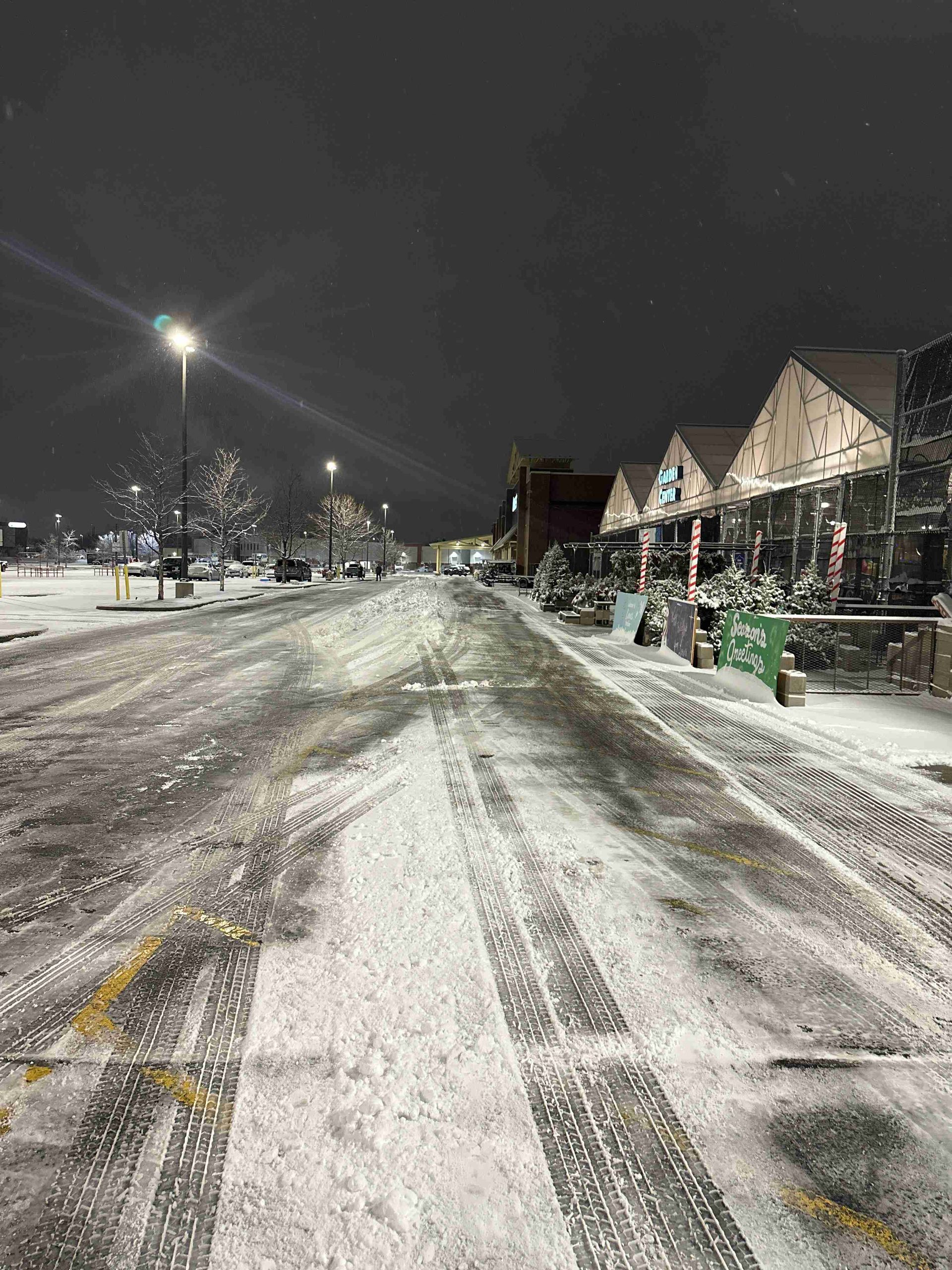 Snow-covered residential street at night with houses and streetlights.