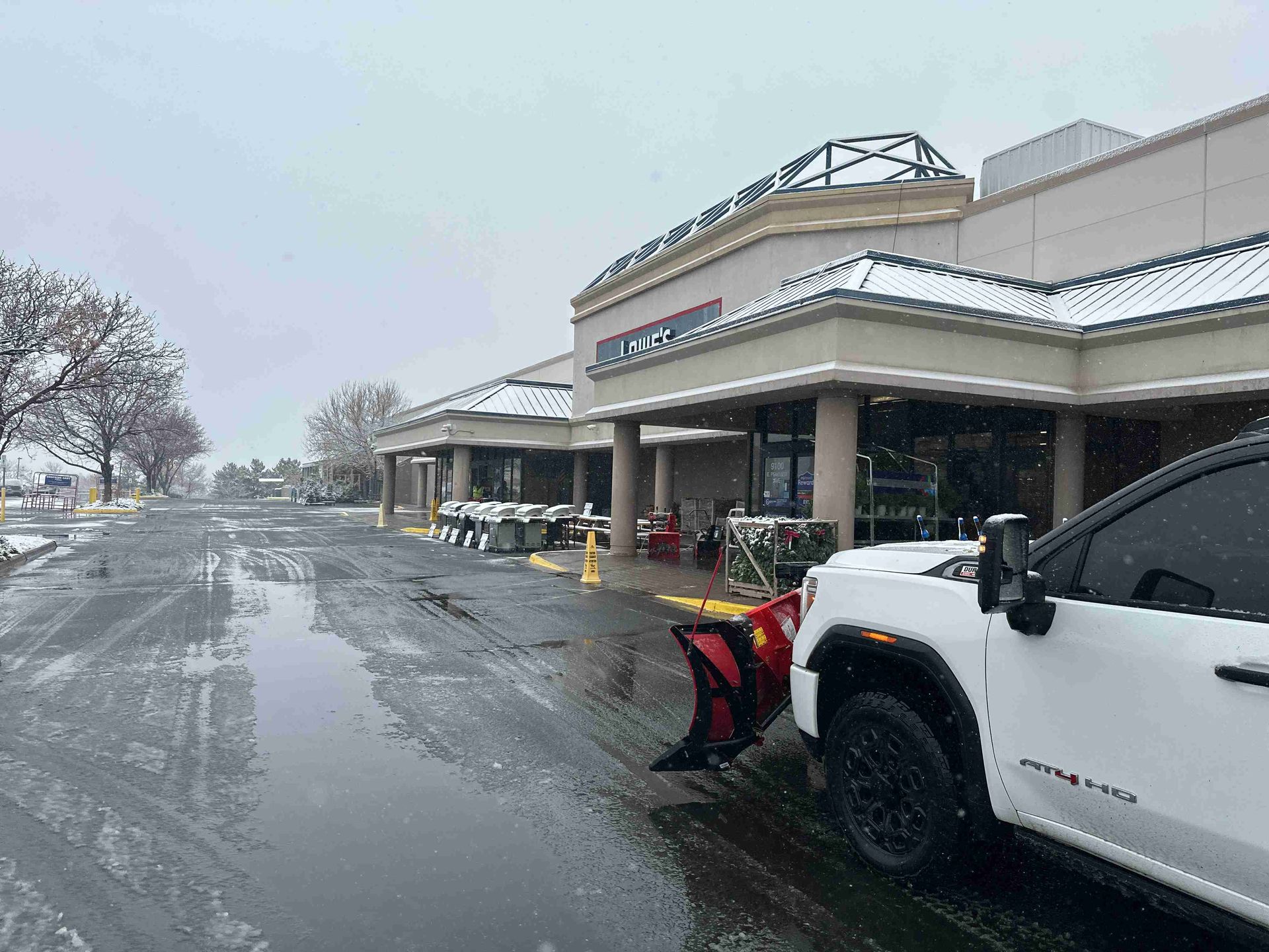 Snowy parking lot outside a storefront, with a white truck and slushy pavement under overcast skies