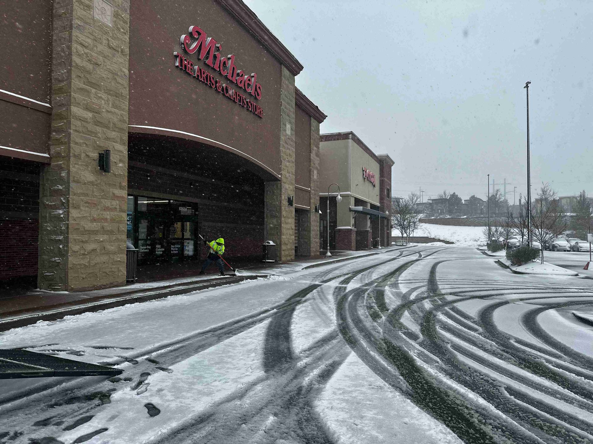 Snowy parking lot outside a store with tire tracks and a person near the entrance
