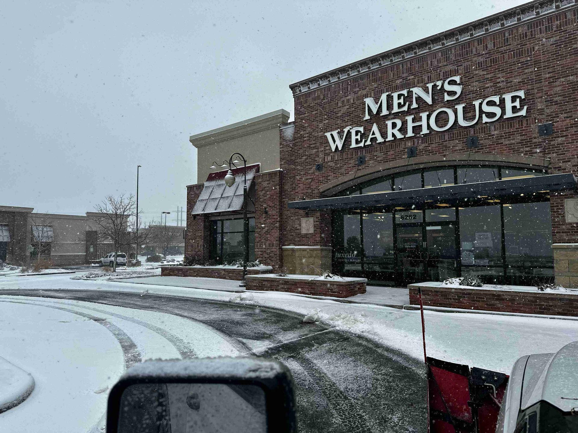 Snowy Men’s Wearhouse storefront with parked cars and falling snow