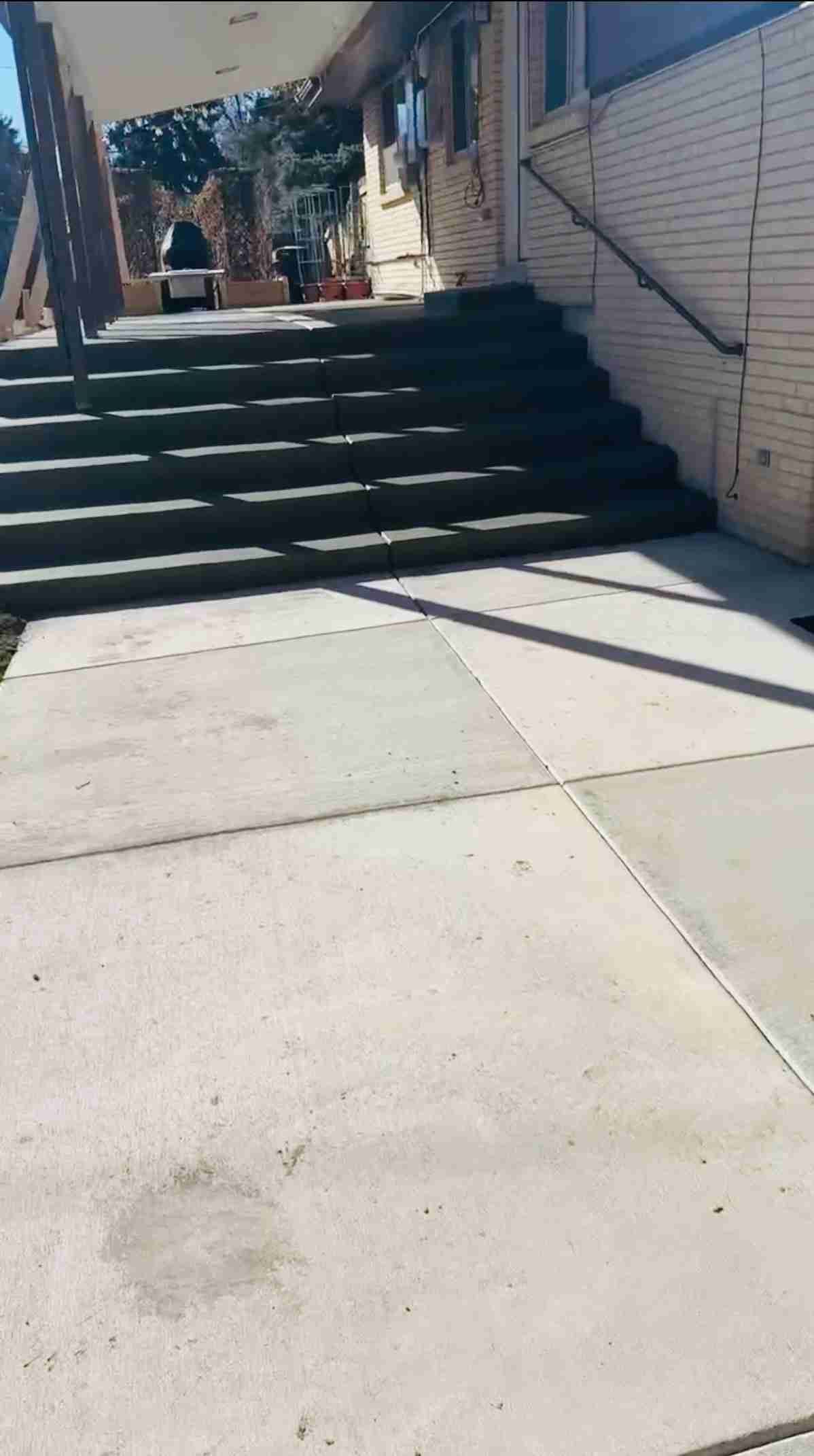 Concrete ramp leading to dark steps beside a white brick wall in bright sunlight.