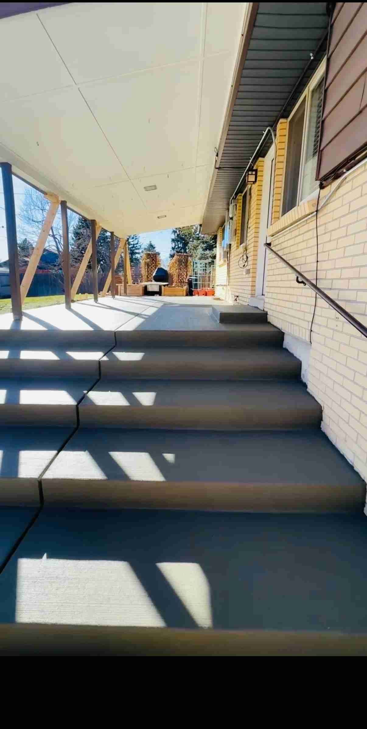 Stairway under a covered walkway with sunlight and shadows, leading up to a building entrance.