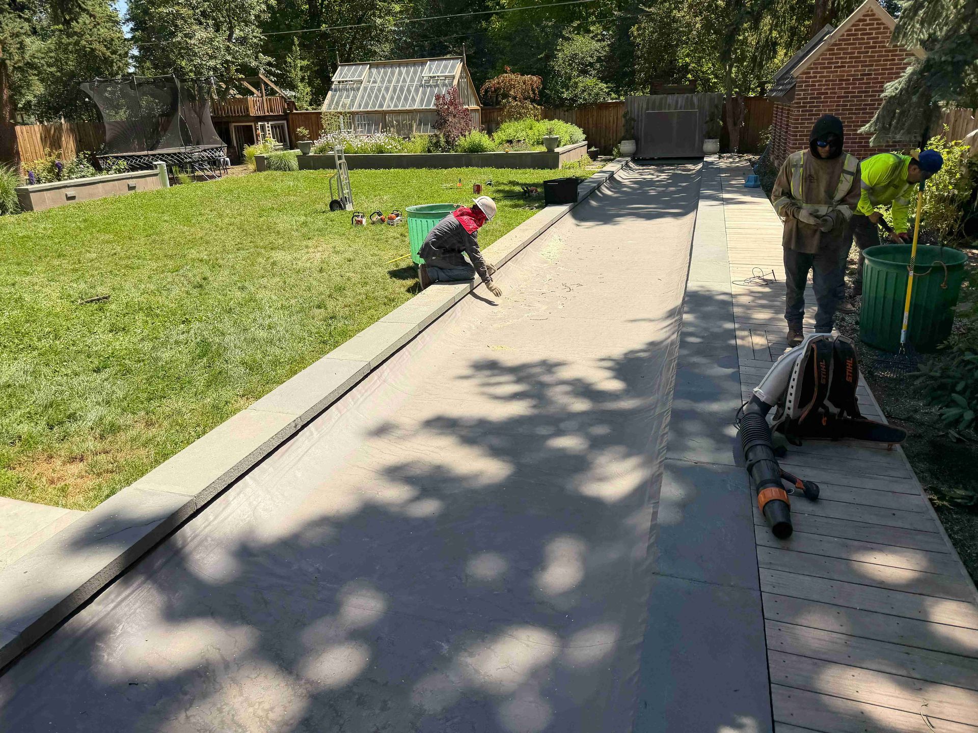 Workers installing a walkway beside a grassy yard, with tools and supplies along the path.
