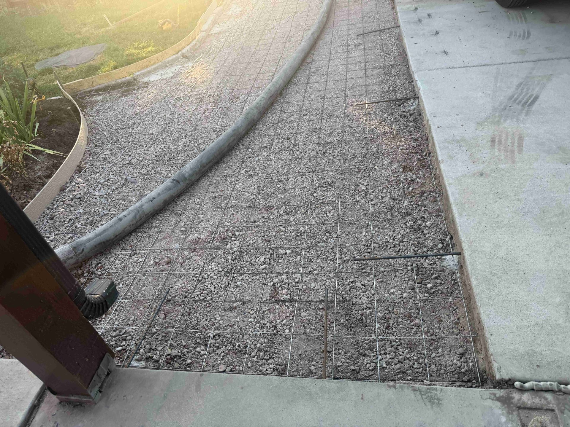 Curved gravel walkway beside a concrete path, with a dark handrail and sunlight at the top left.