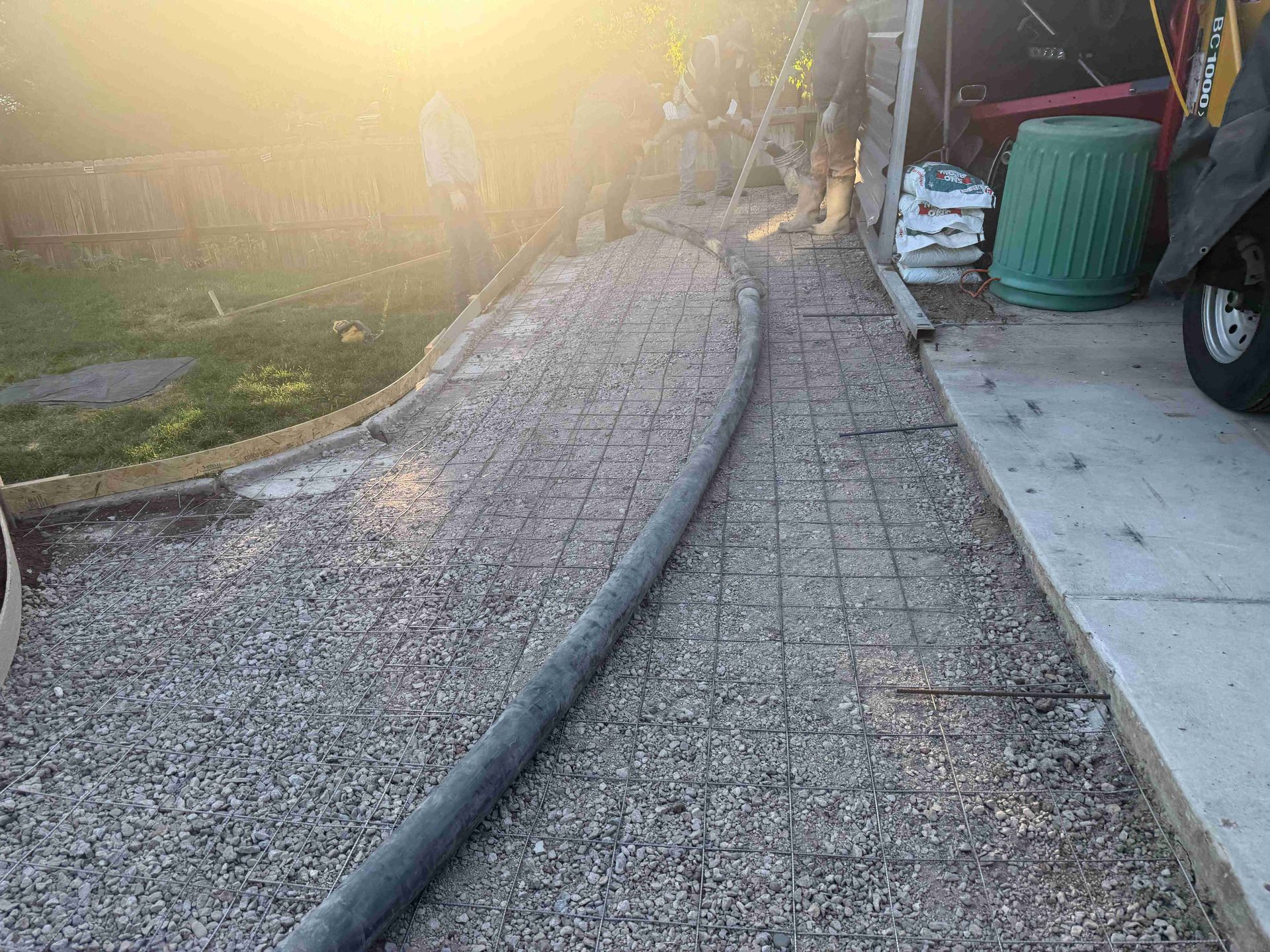 Curved concrete walkway beside a gravel yard, with sun glare and a red car on the right.