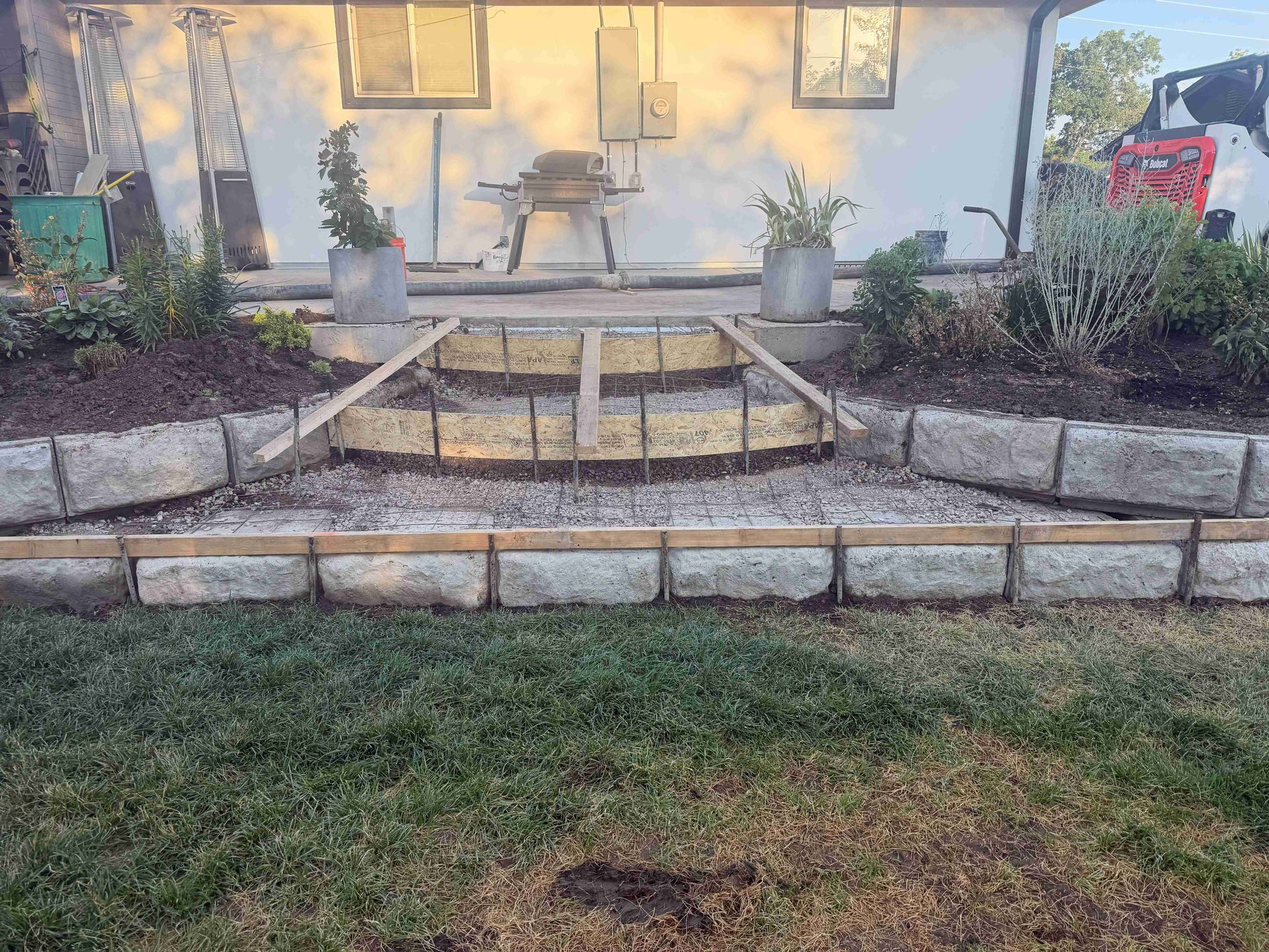 Front yard patio with stone steps, retaining walls, potted plants, and a glass table on a porch.