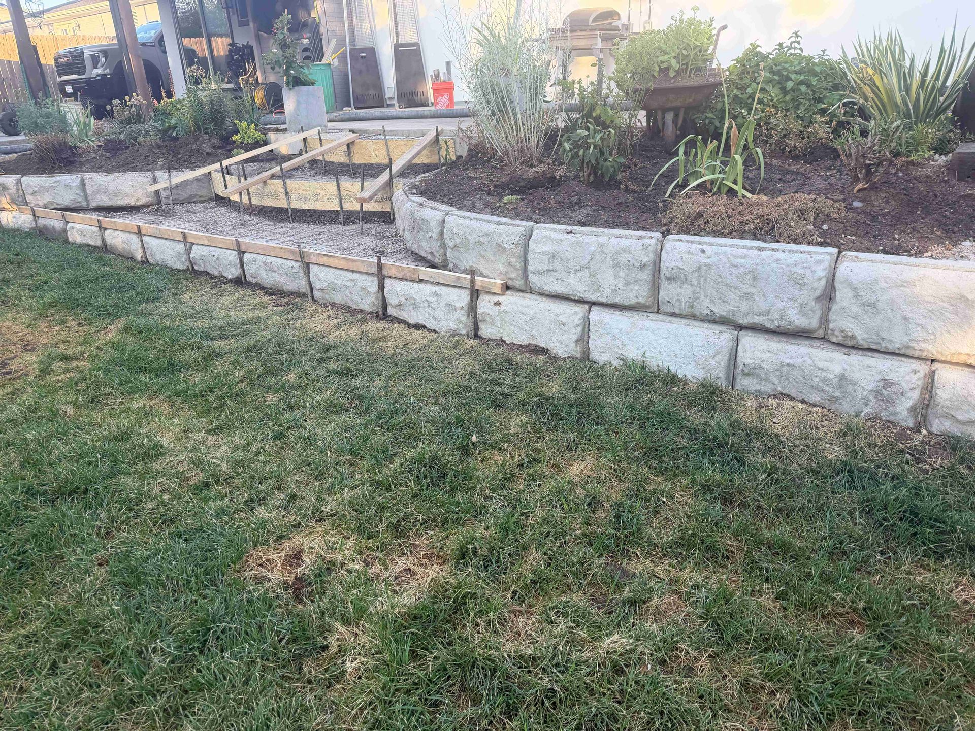 Raised stone garden beds beside a grassy yard at sunset