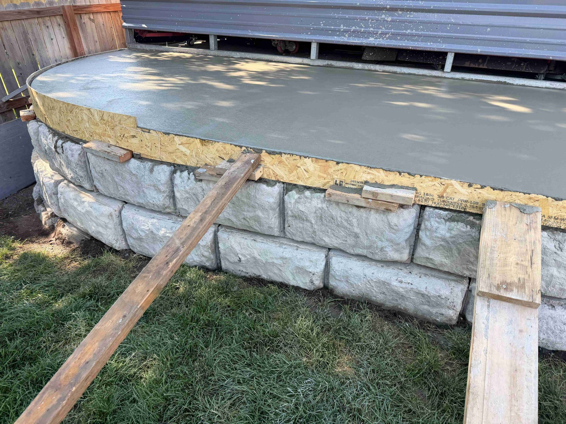 Stone retaining wall with concrete top and wooden support beams around a raised deck in a yard