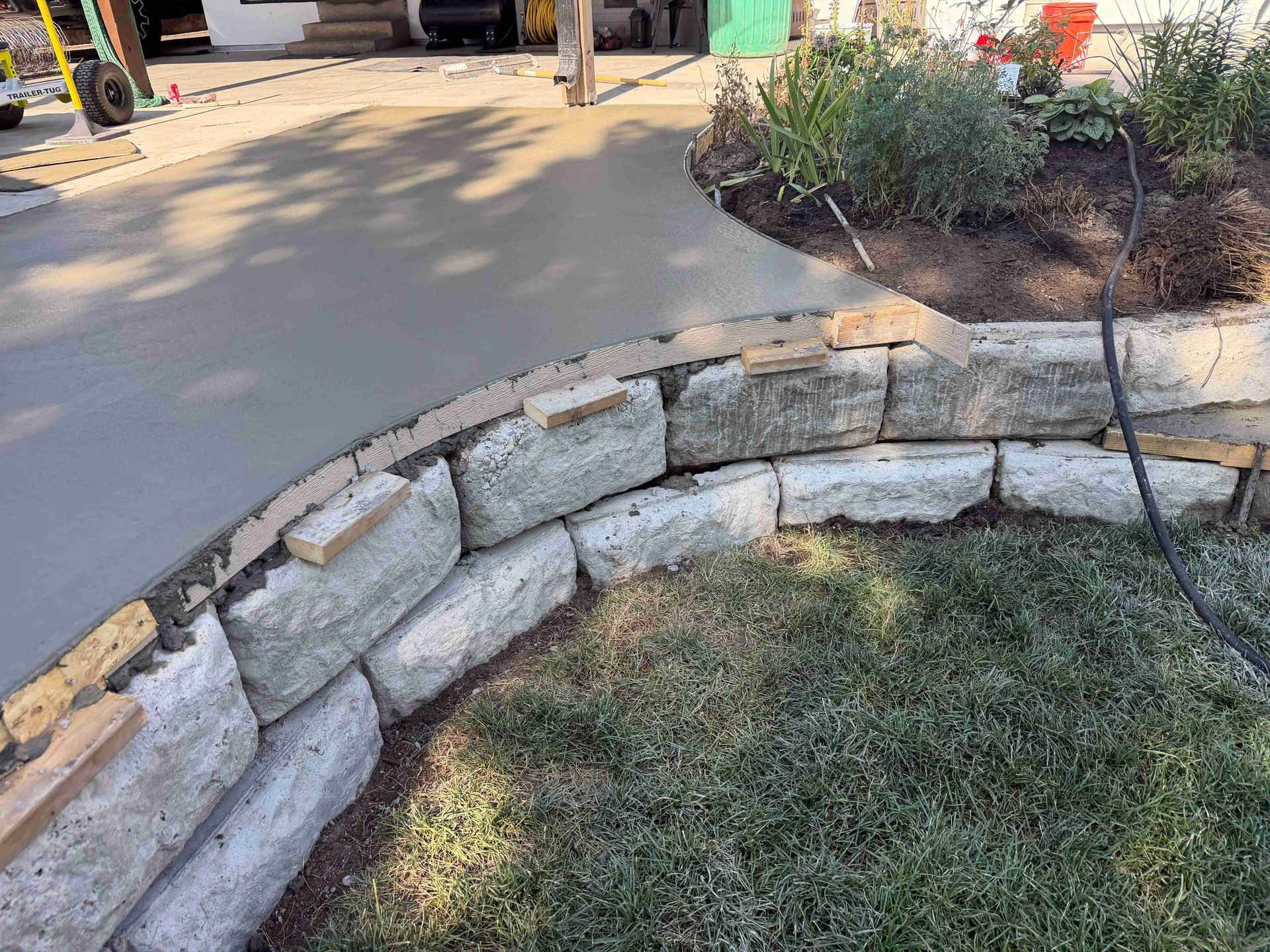 Curved stone garden border beside a concrete walkway and grass lawn in sunlight