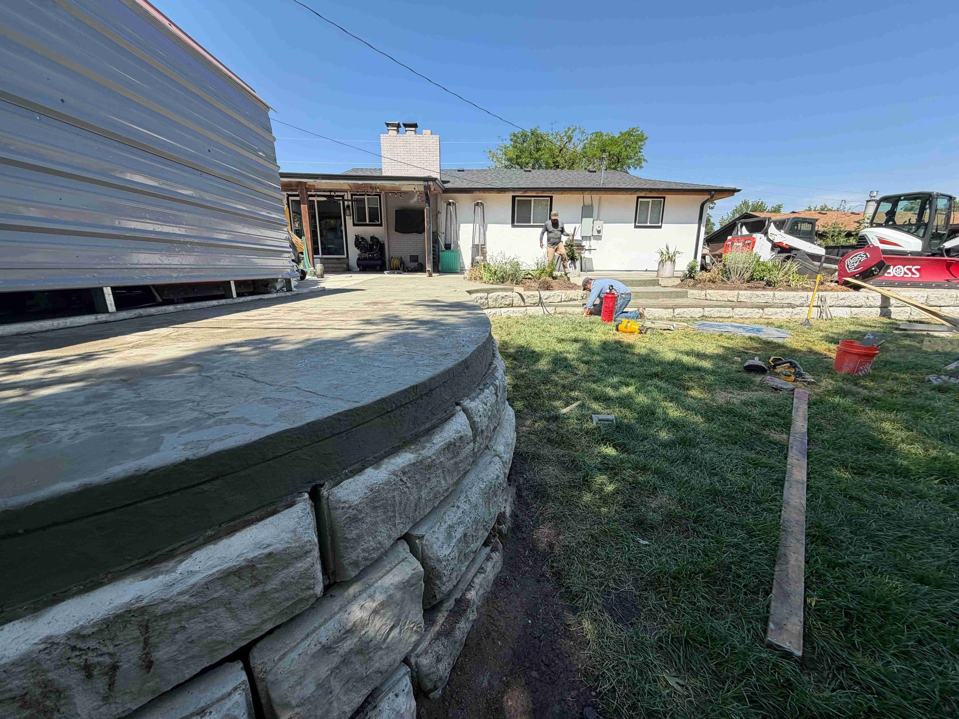 Backyard construction site with stacked concrete blocks, a house, and scattered tools and materials