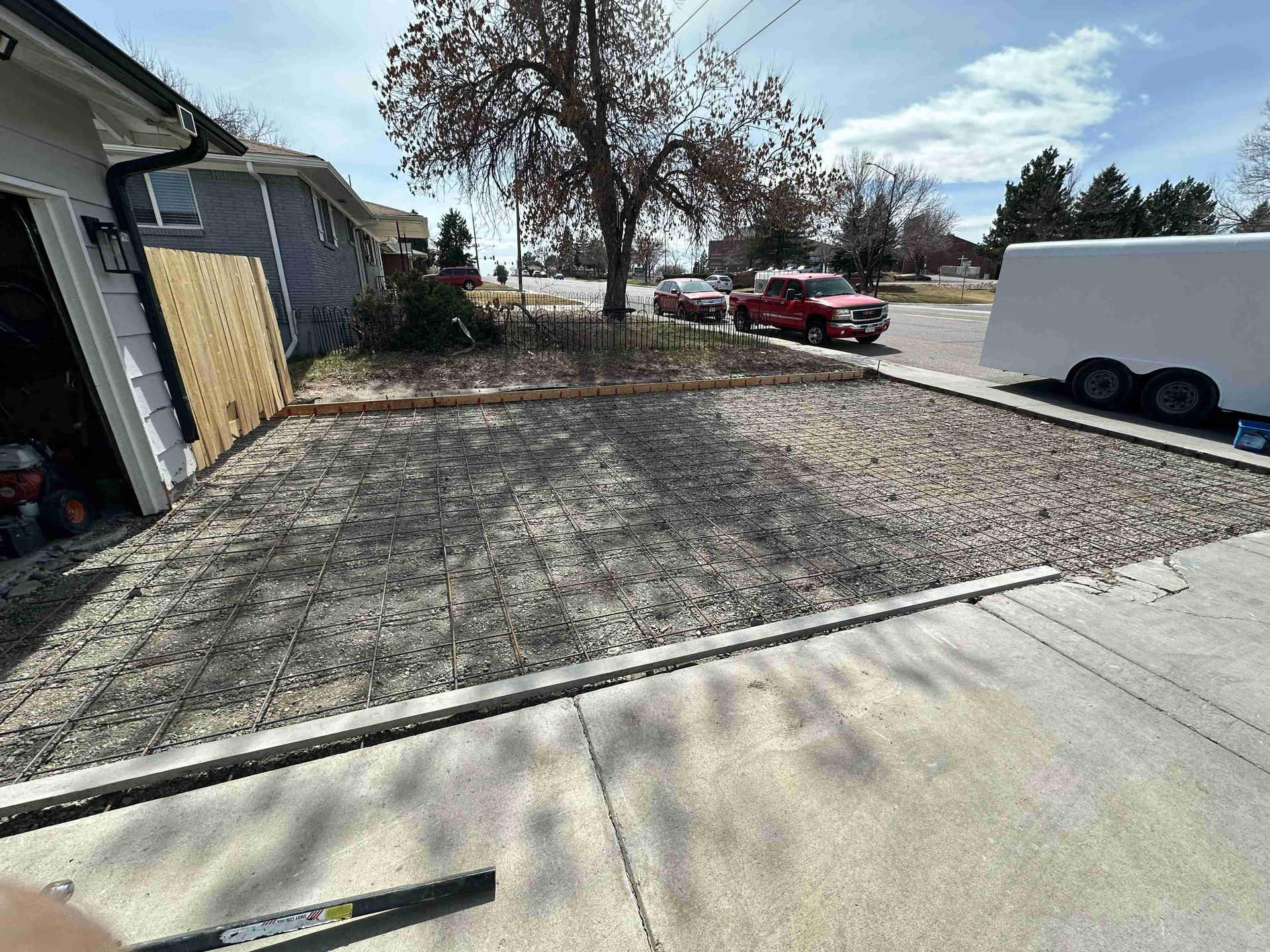 Empty gravel driveway beside a house, with a red car and white trailer on a sunny day.