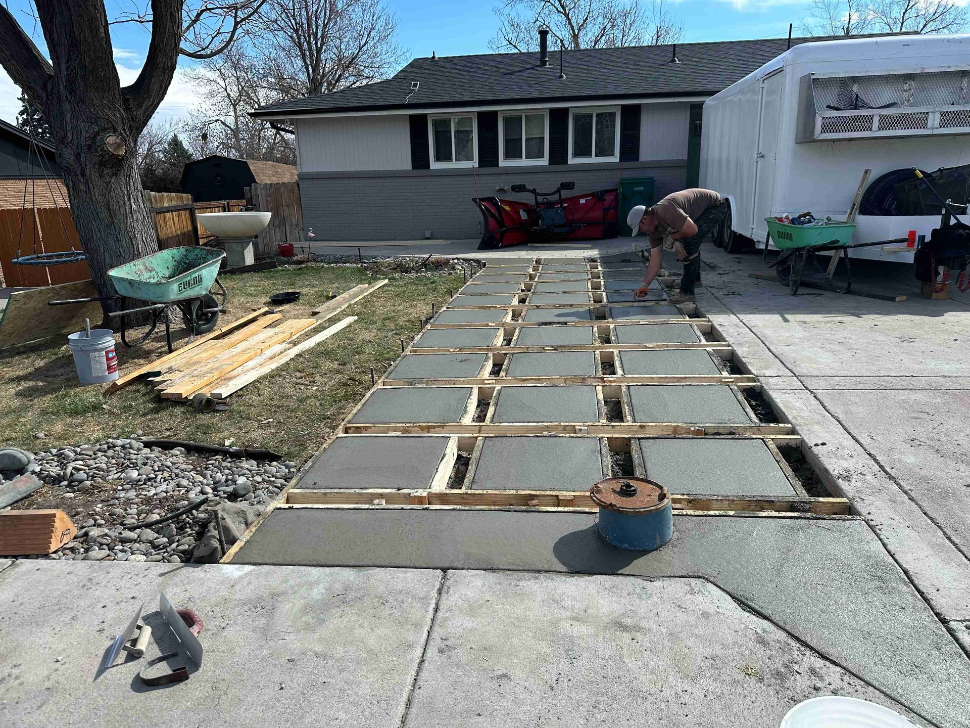 Workers building a concrete walkway in a front yard beside a house, with forms and tools laid out.