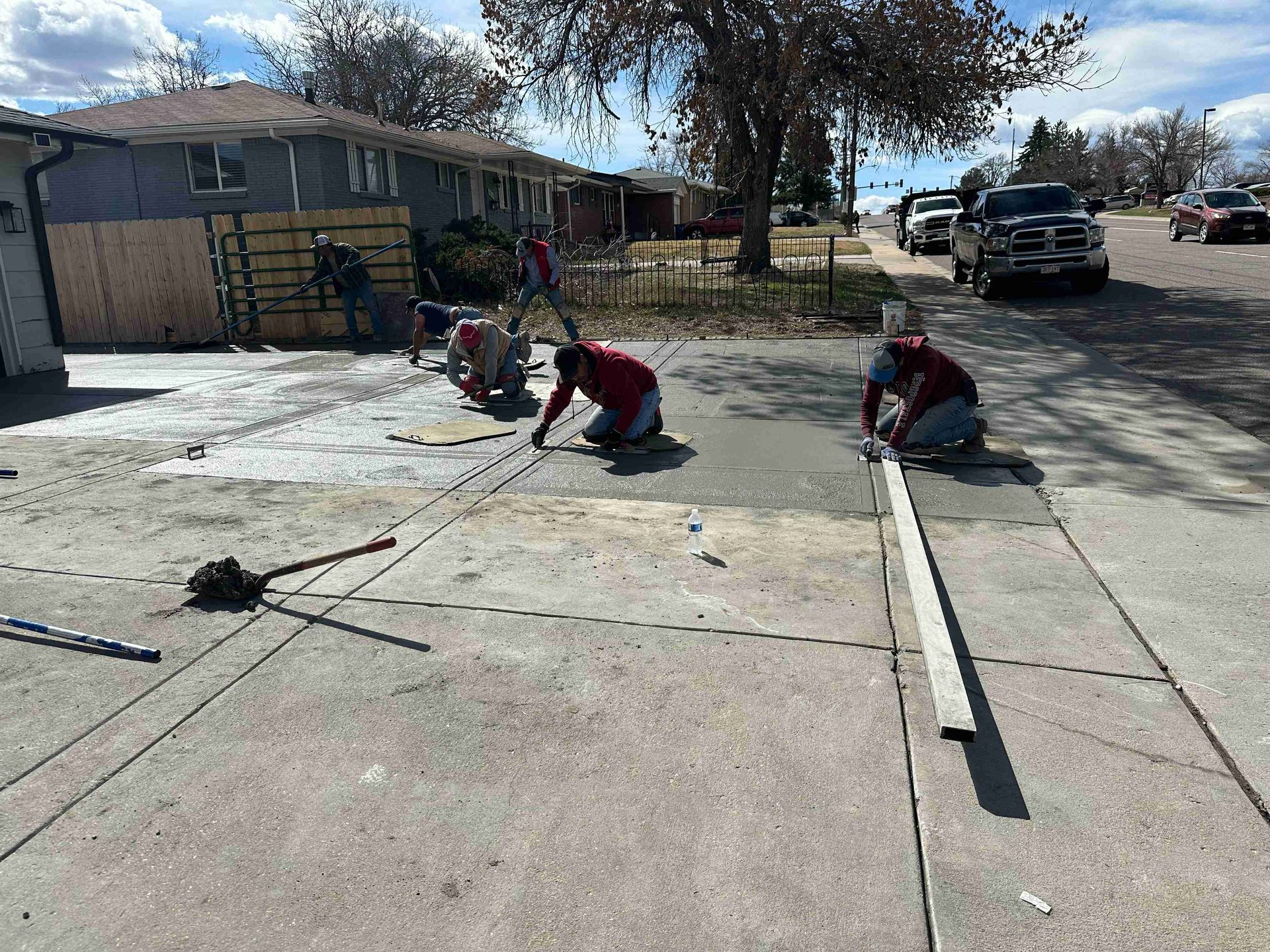 Workers repairing a cracked concrete driveway with tools and long boards on a sunny residential street