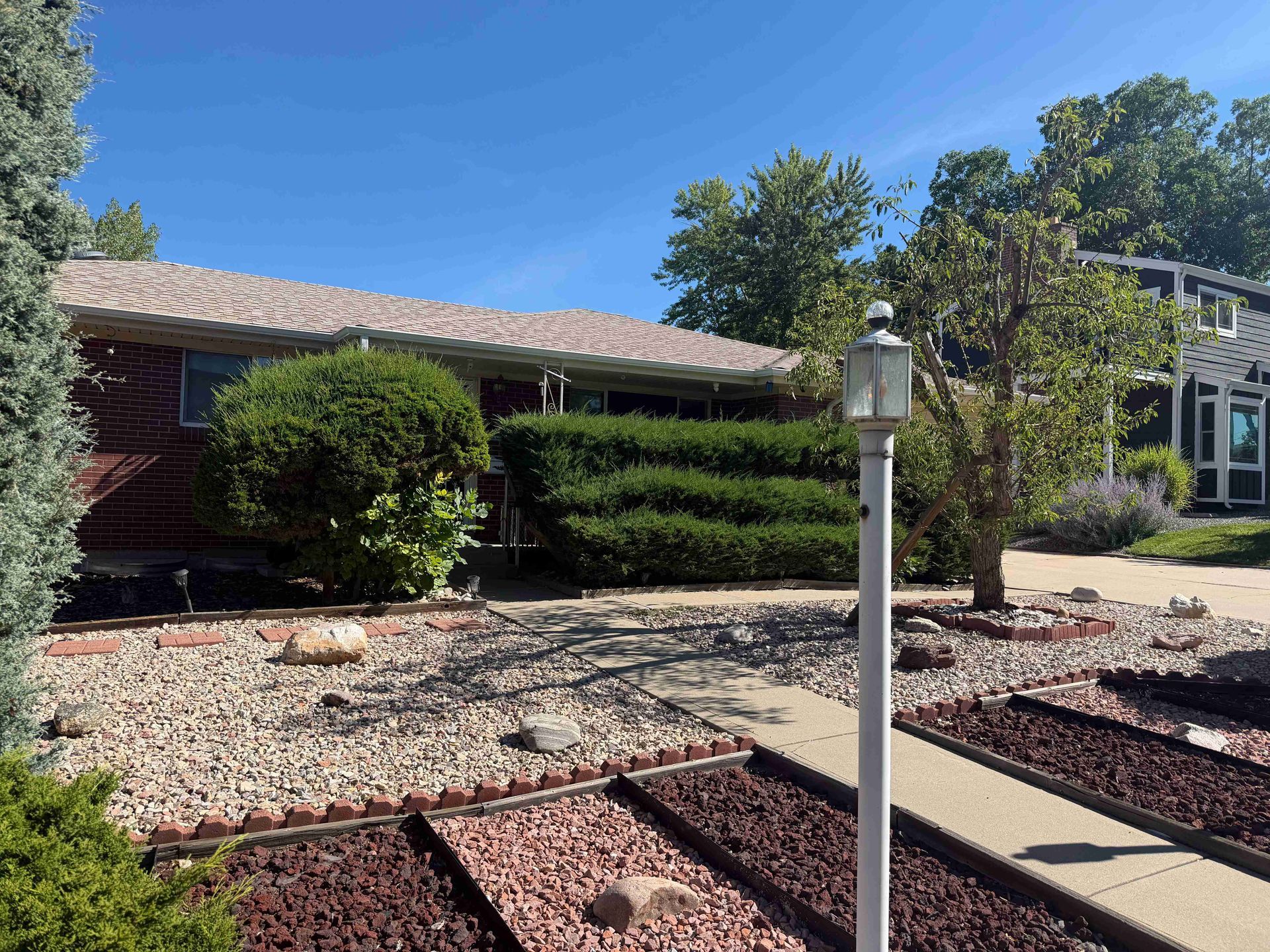 Sunny front yard with desert landscaping, a lamp post, and a house under a blue sky.