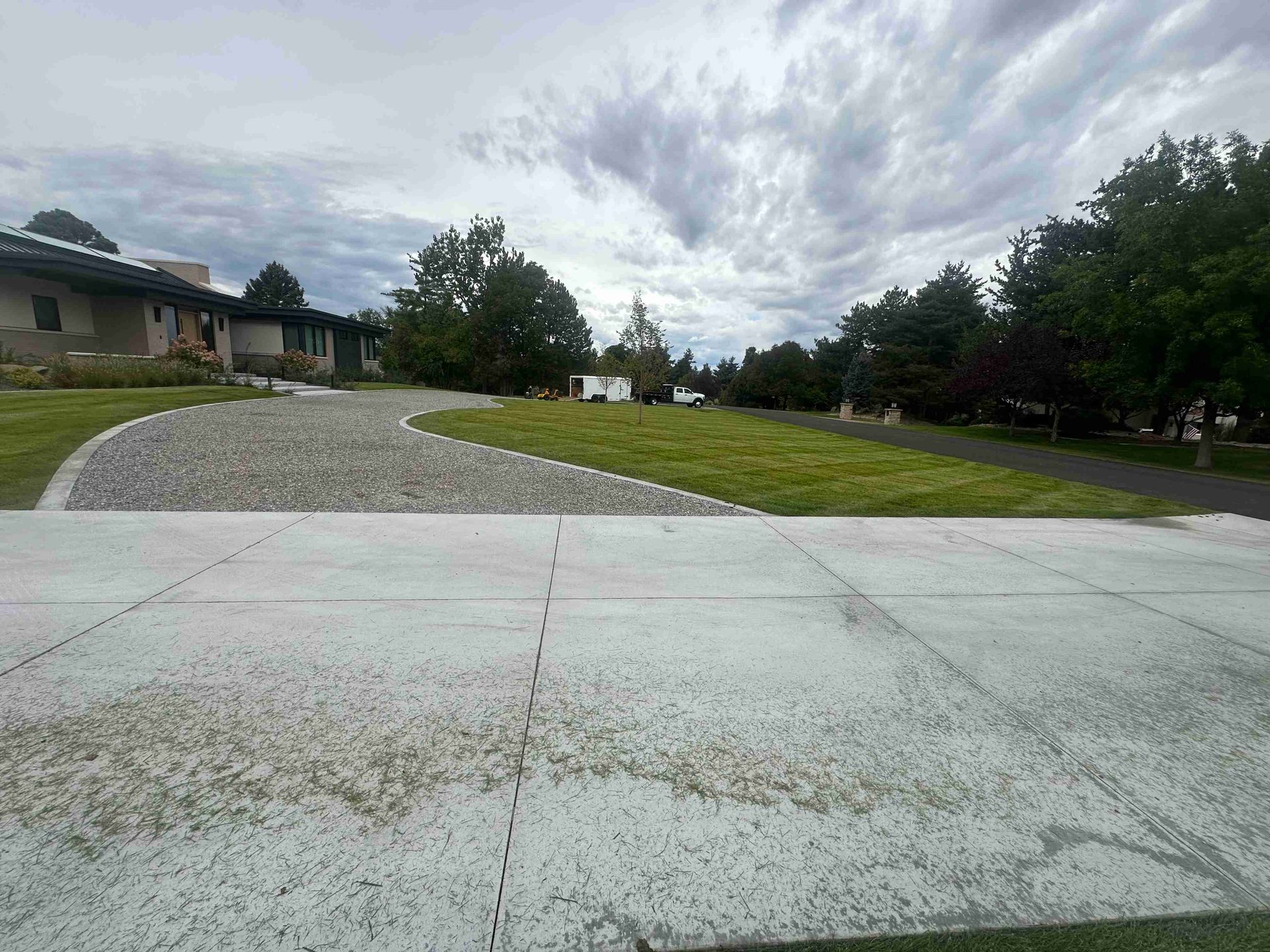 Wide driveway leading to a house, with a curved gravel path, green lawn, and cloudy sky.
