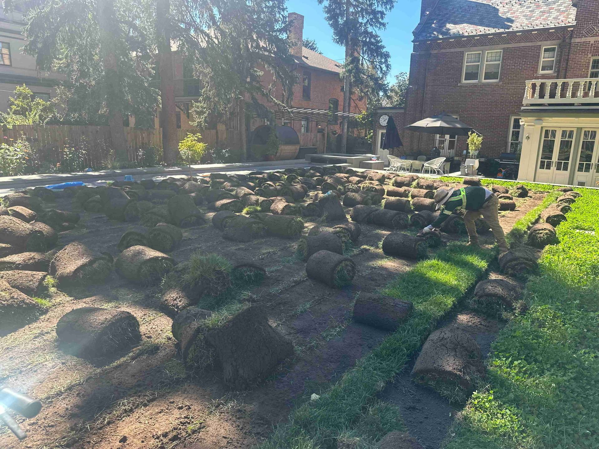Stone-lined garden bed with dark soil and a small waterfall beside a brick house in sunlight