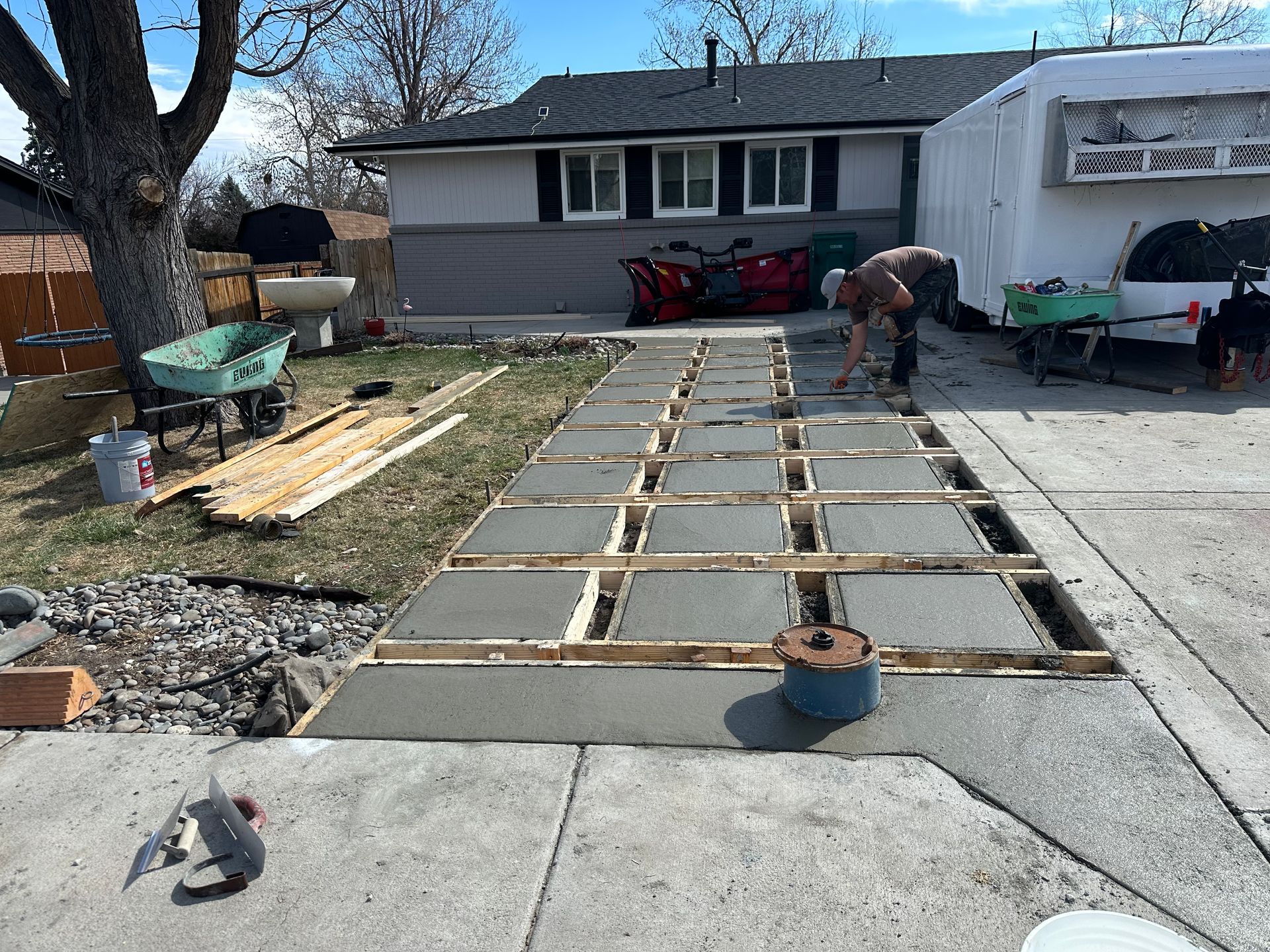 Concrete walkway under construction in front of a house, with wooden forms and workers.