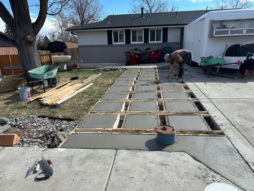 Concrete walkway under construction in front of a house, with wooden forms and workers.