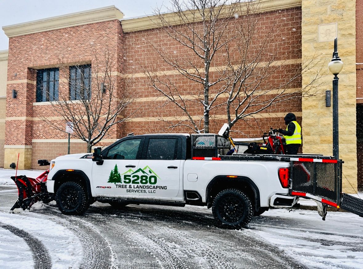 Snowplow truck clearing snow in front of a brick building on a snowy street