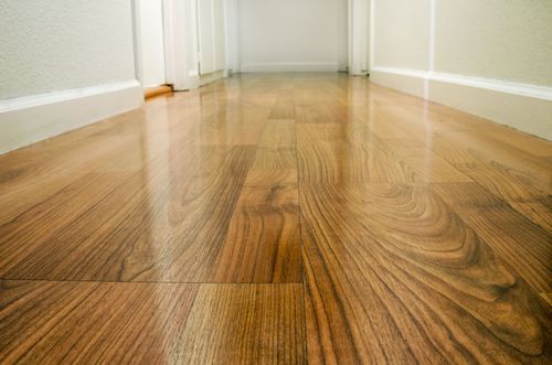 Empty hallway with glossy wood flooring and white baseboards viewed from floor level