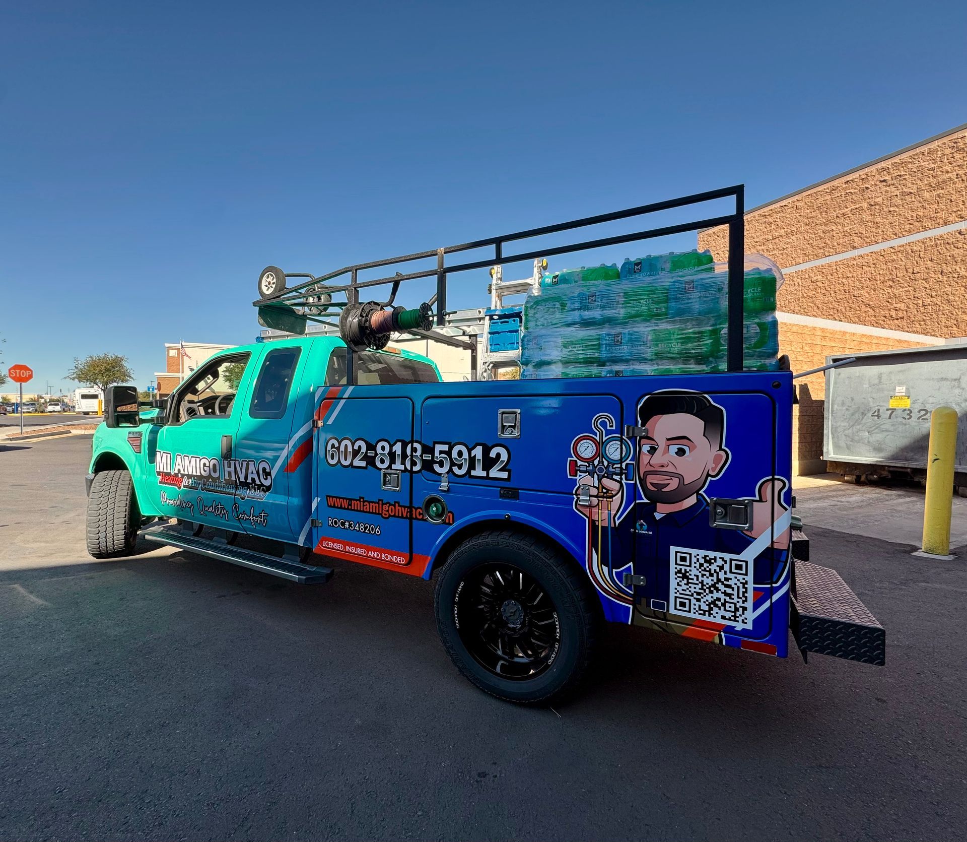 A teal and blue service truck with a ladder rack, carrying water cases and featuring a cartoon mascot and phone number.