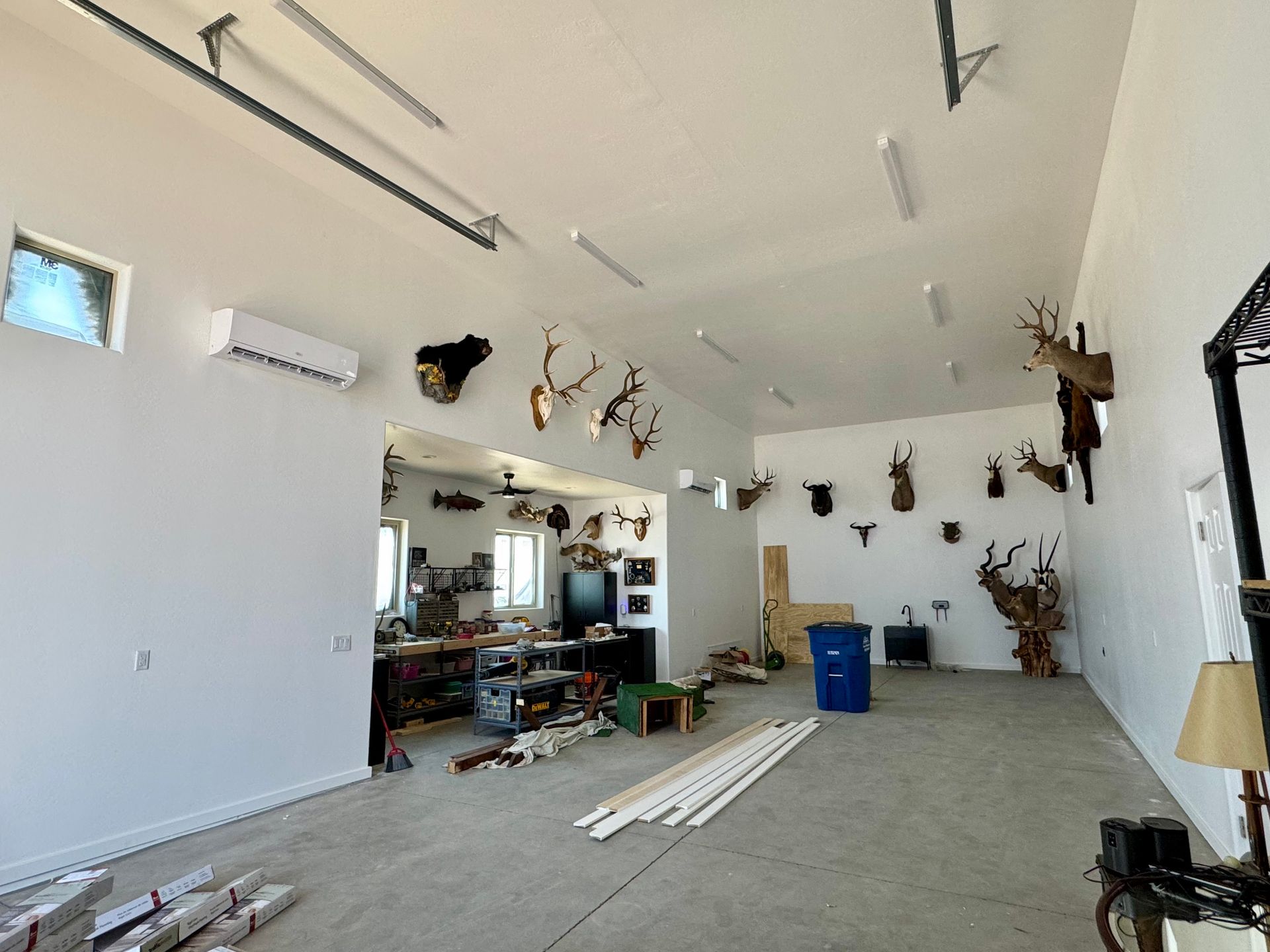 A large garage interior features white walls decorated with many animal head mounts, a workbench area, and concrete floors.