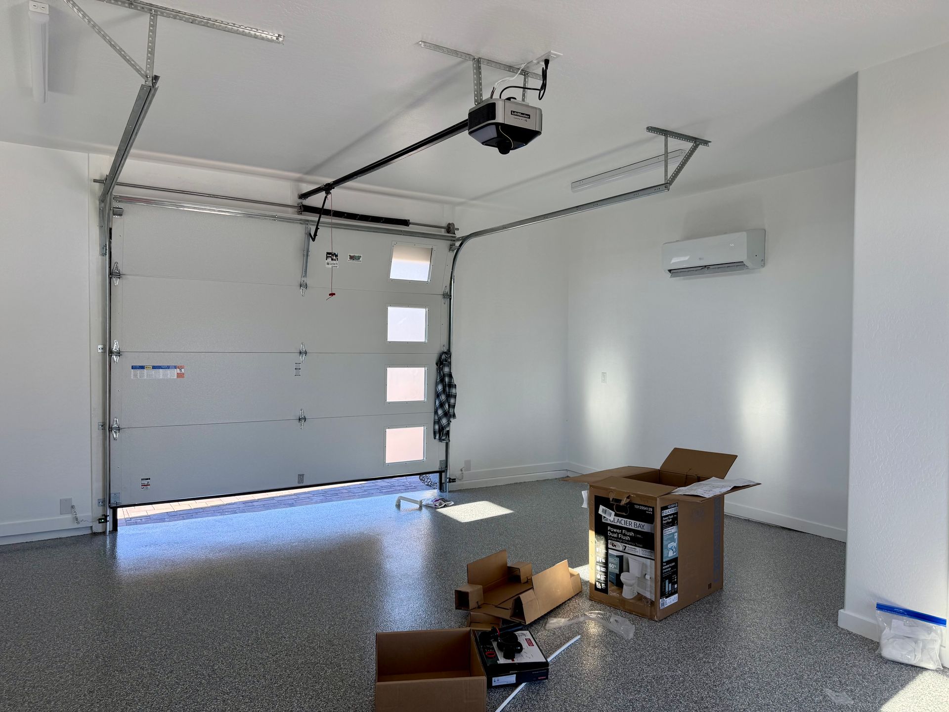 A clean, empty garage with white walls, a speckled floor, a closed garage door, and cardboard boxes on the floor.