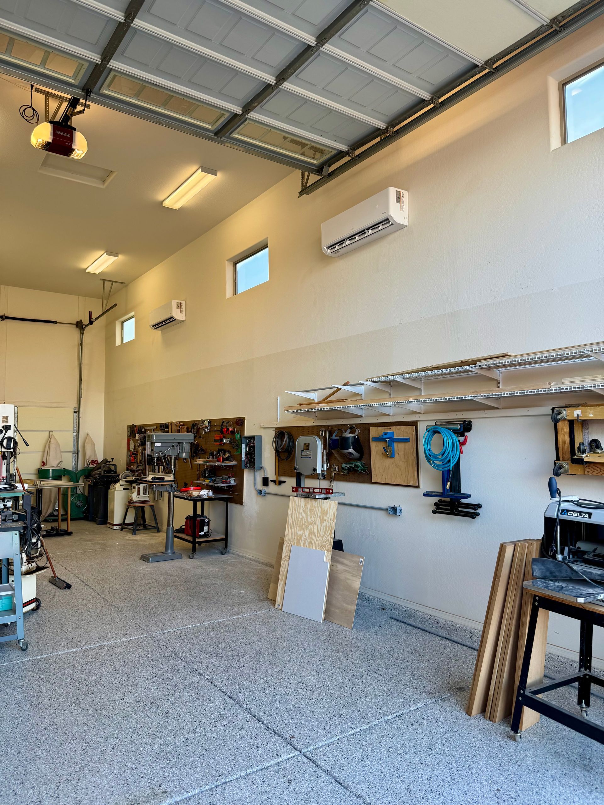 A well-organized workshop garage with tools hung on walls, a speckled floor, and two wall-mounted air conditioning units.