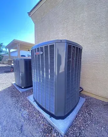 Two outdoor HVAC condenser units sit on a gravel ground; one unit has its top fan housing detached and tilted open.