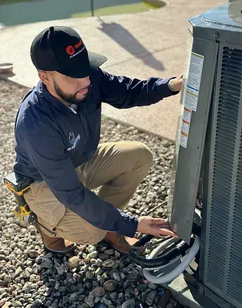 Two tan outdoor air conditioning units on concrete pads next to a red stucco exterior wall.