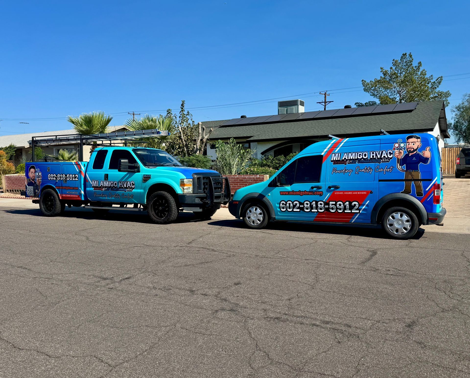 Two branded blue utility vehicles, a truck and a van, parked on a residential street under a clear blue sky.