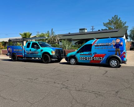 Two branded blue utility vehicles, a truck and a van, parked on a residential street under a clear blue sky.