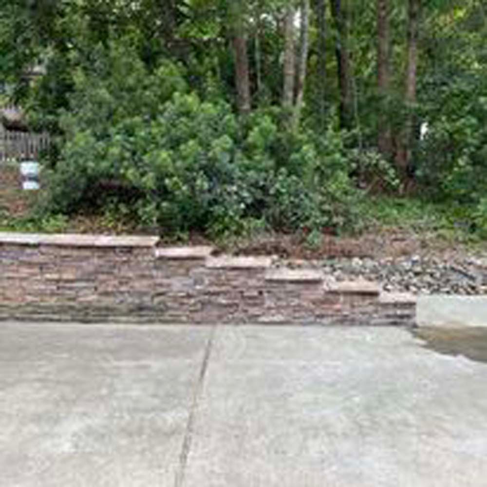 A stone wall is surrounded by trees and a concrete driveway.